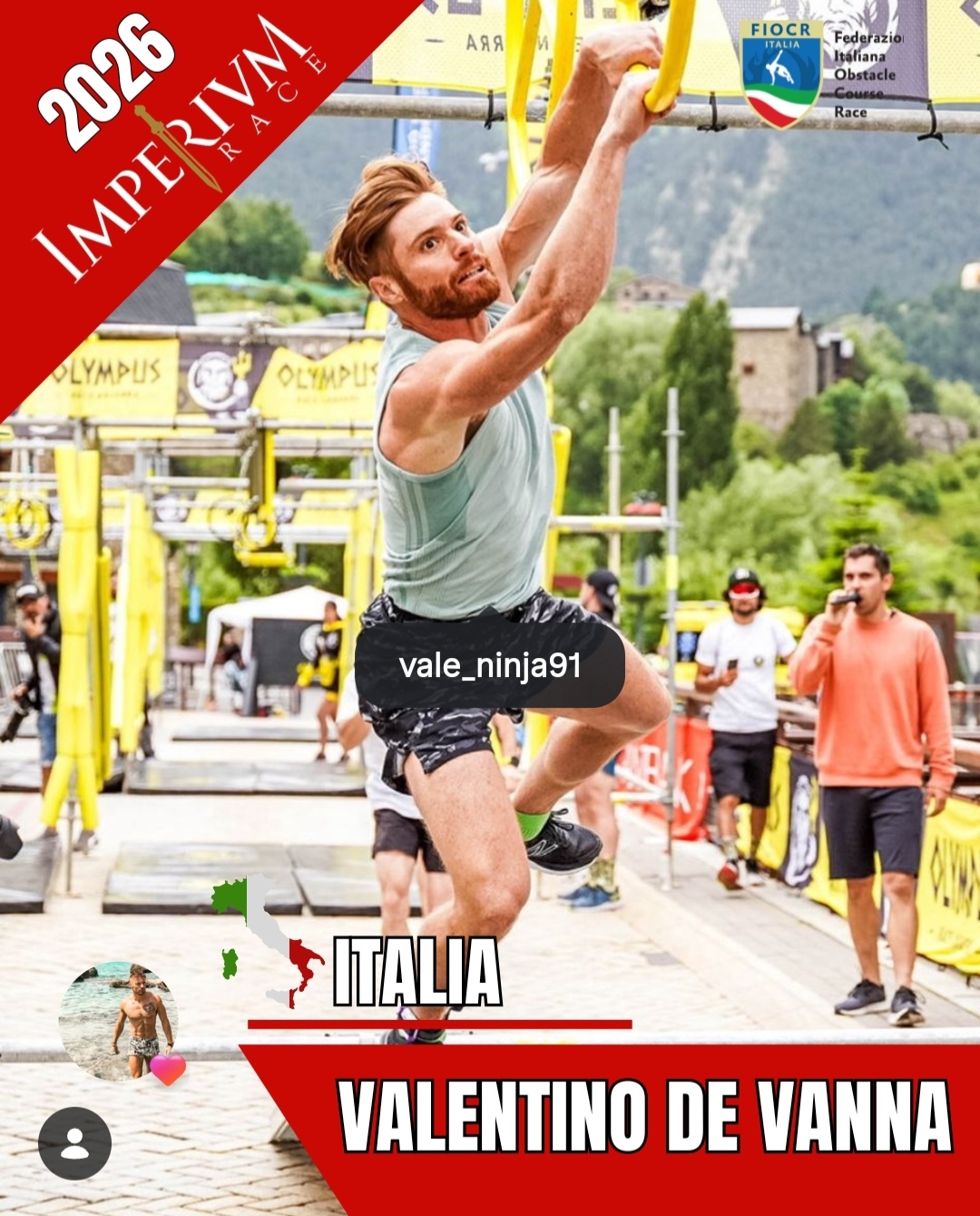 Atleta solleva un braccio in posa durante gara a ostacoli, sfondo verde e cartelloni “Italia”.
Valentino De Vanna